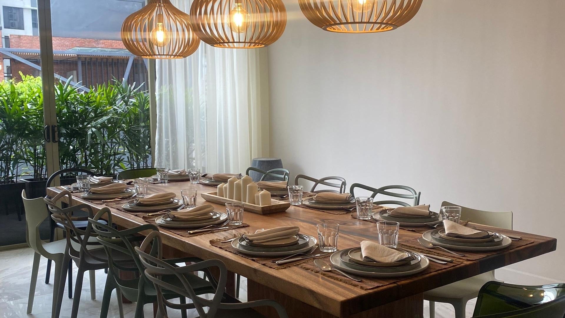 Dining room with a long wooden table set for dinner, featuring modern chairs and decorative pendant lights.